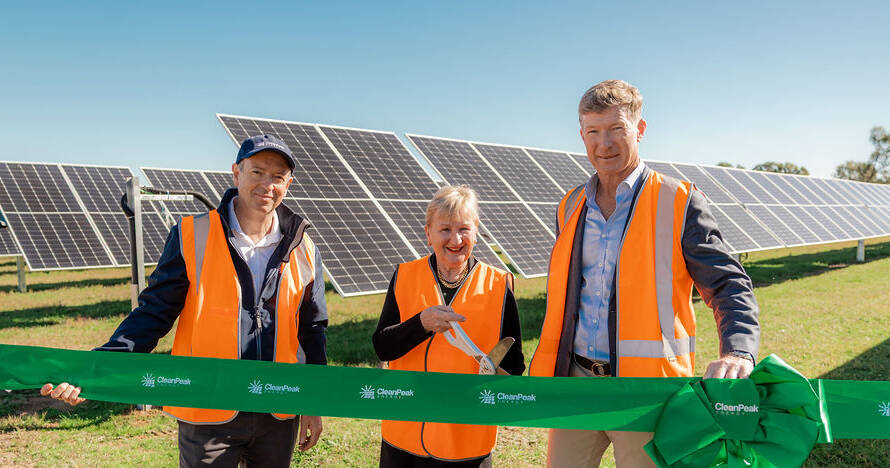 Three people in high-vis vests cutting green ribbon in front of solar farm