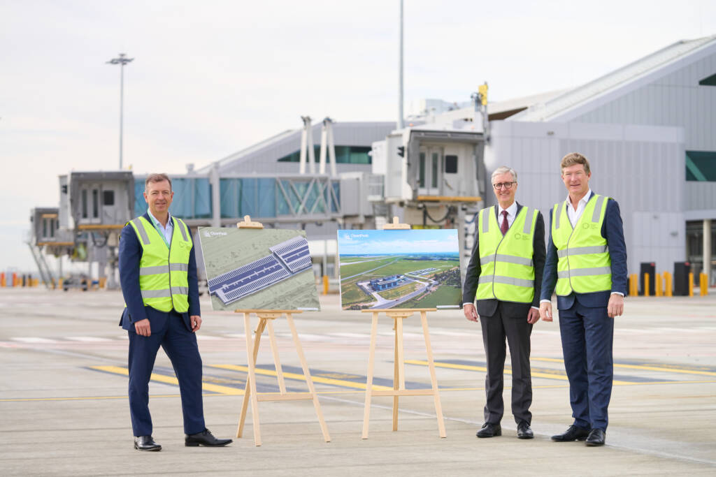 Three men in high vis vests on the tarmac in front of airport terminal